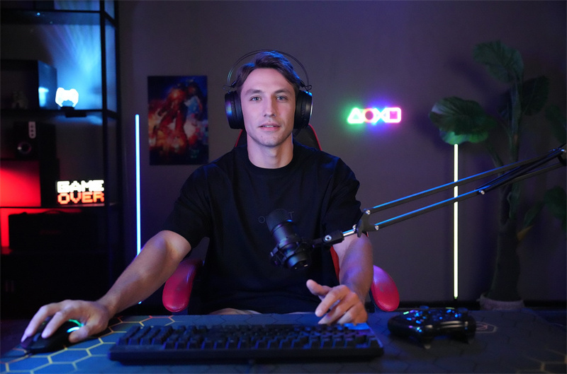 Seorang streamer game Indonesia sedang siaran langsung dari studio gaming dengan perlengkapan lengkap seperti mikrofon, headset, dan pencahayaan RGB.